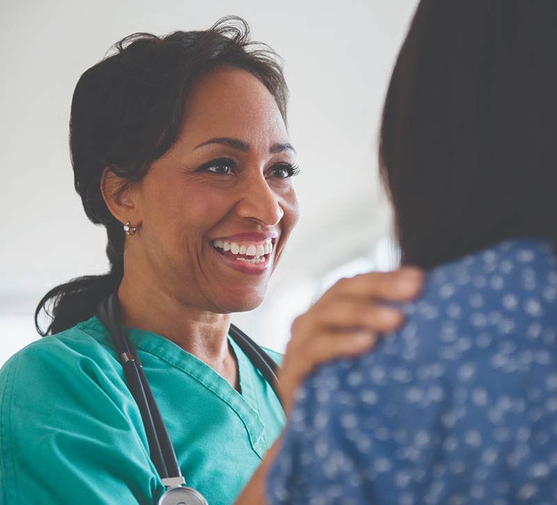 Smiling healthcare professional interacting with a patient, wearing scrubs and a stethoscope.