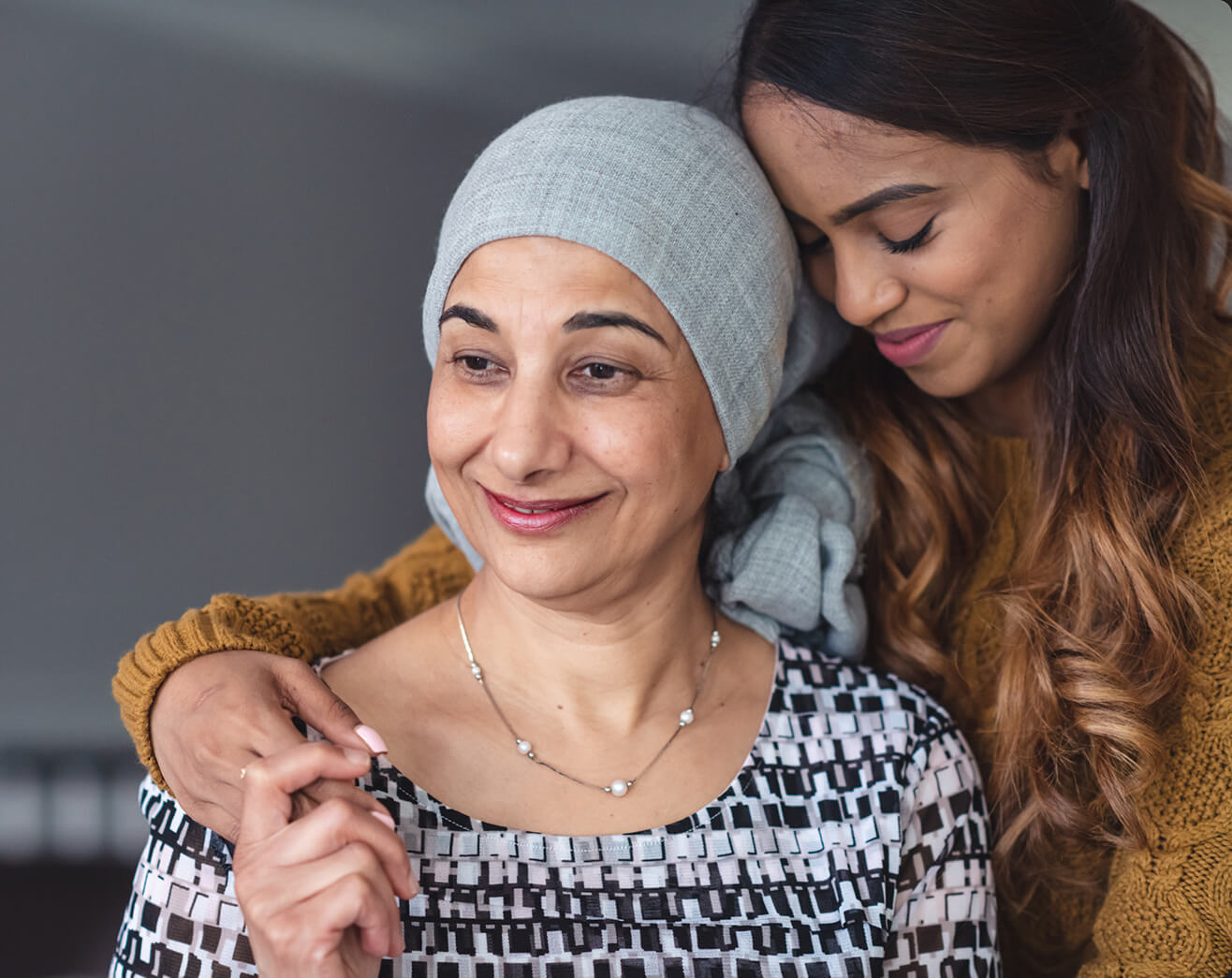 A mother and daughter smiling together, with the mother wearing a headscarf and the daughter in a patterned top.